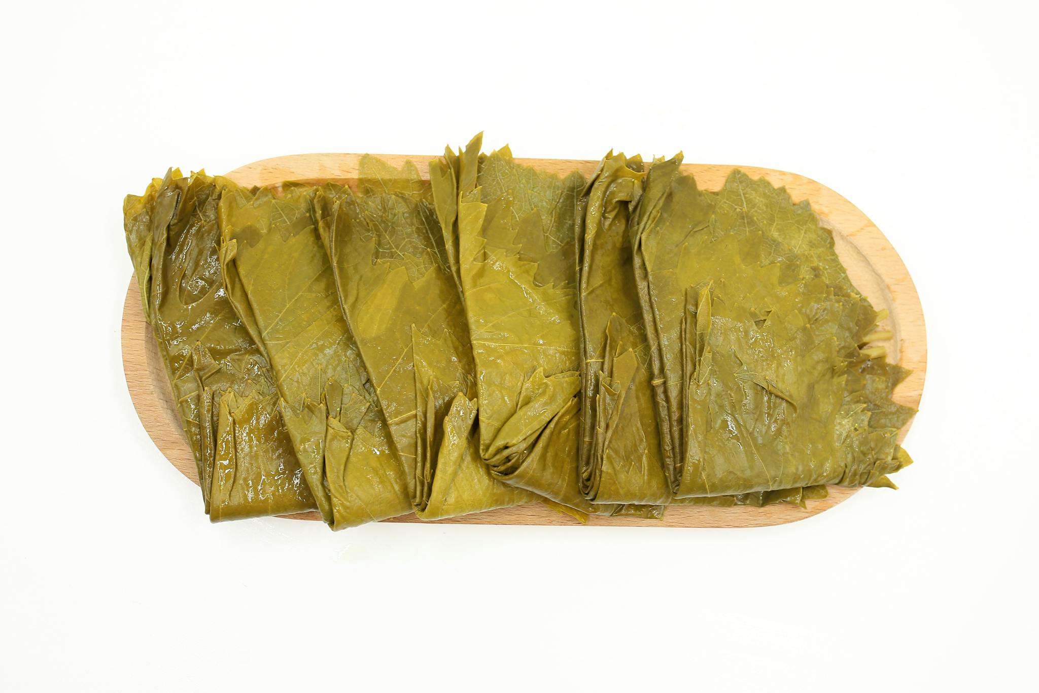 A wooden cutting board topped with fresh grape leaves against a white background, ideal for culinary projects.