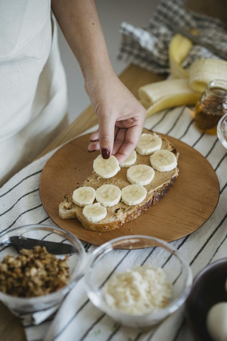 Hand placing banana slices on toasted bread. Perfect healthy breakfast preparation.