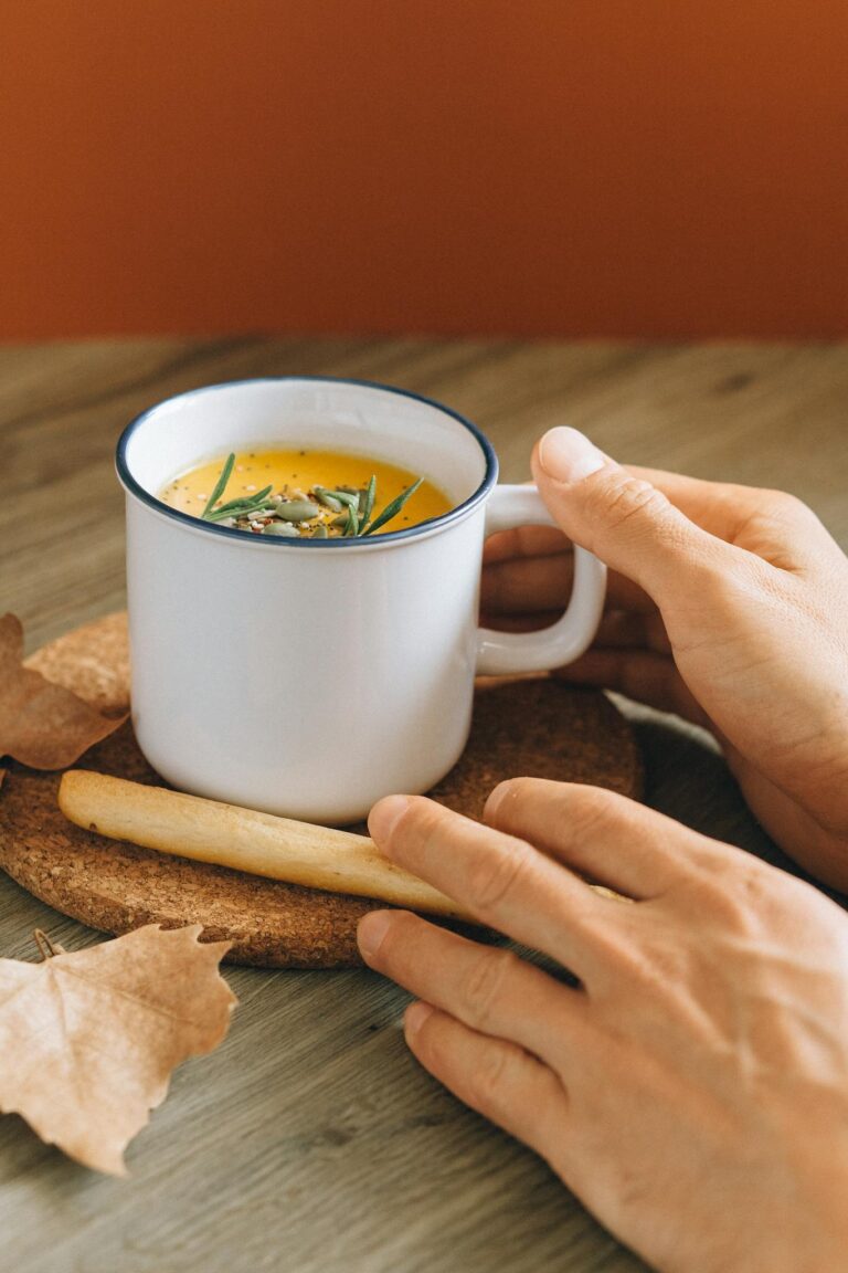Warm homemade pumpkin soup in a mug with a breadstick, perfect for a cozy autumn meal.